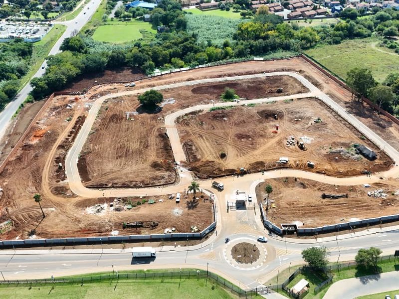 Aerial view of a residential development site featuring established perimeter walls, a gated entrance, and internal road infrastructure under construction.