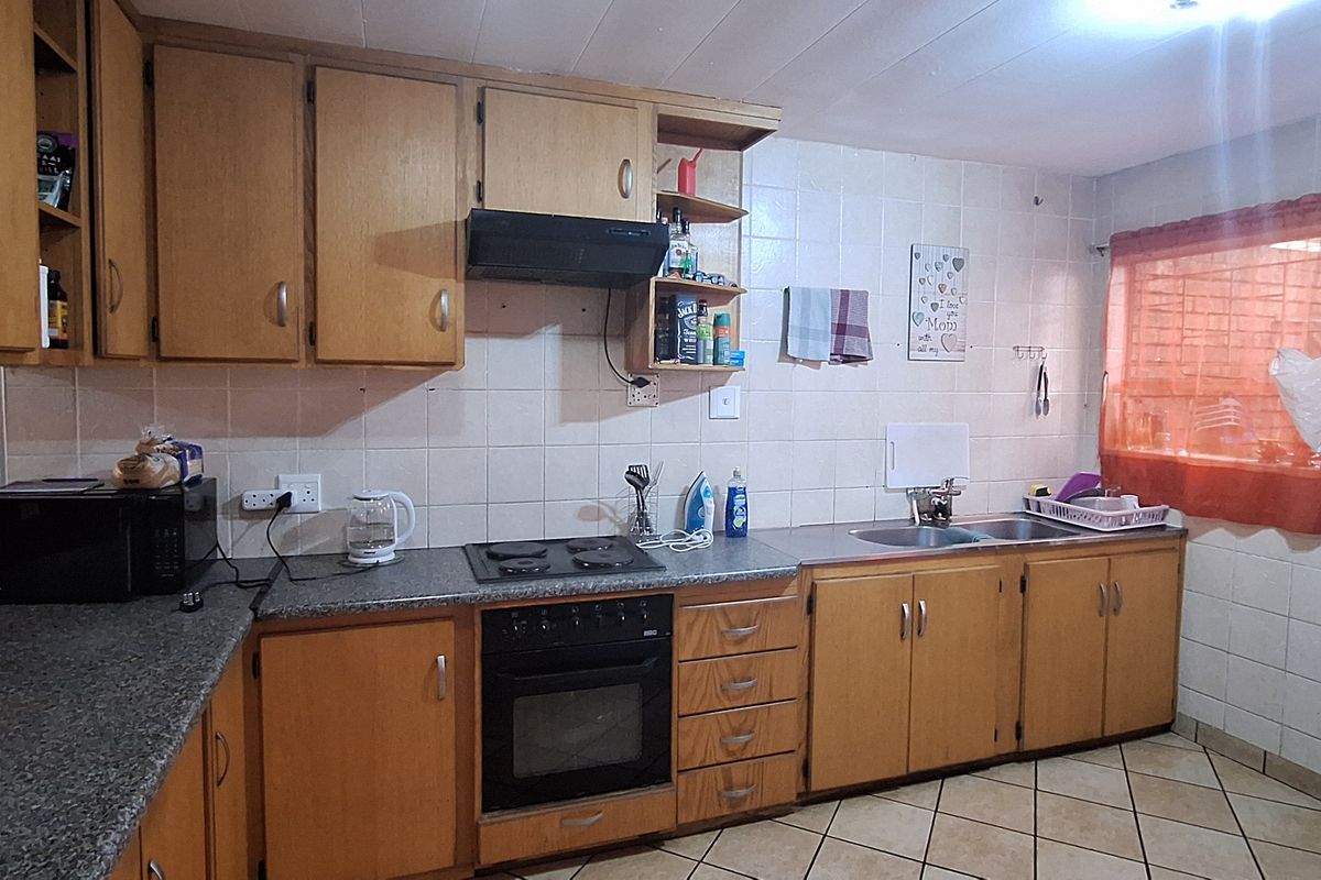 A functional kitchen featuring wooden cabinetry, laminate countertops, a built-in oven, hob, extractor fan, and a double sink with tiled backsplash.