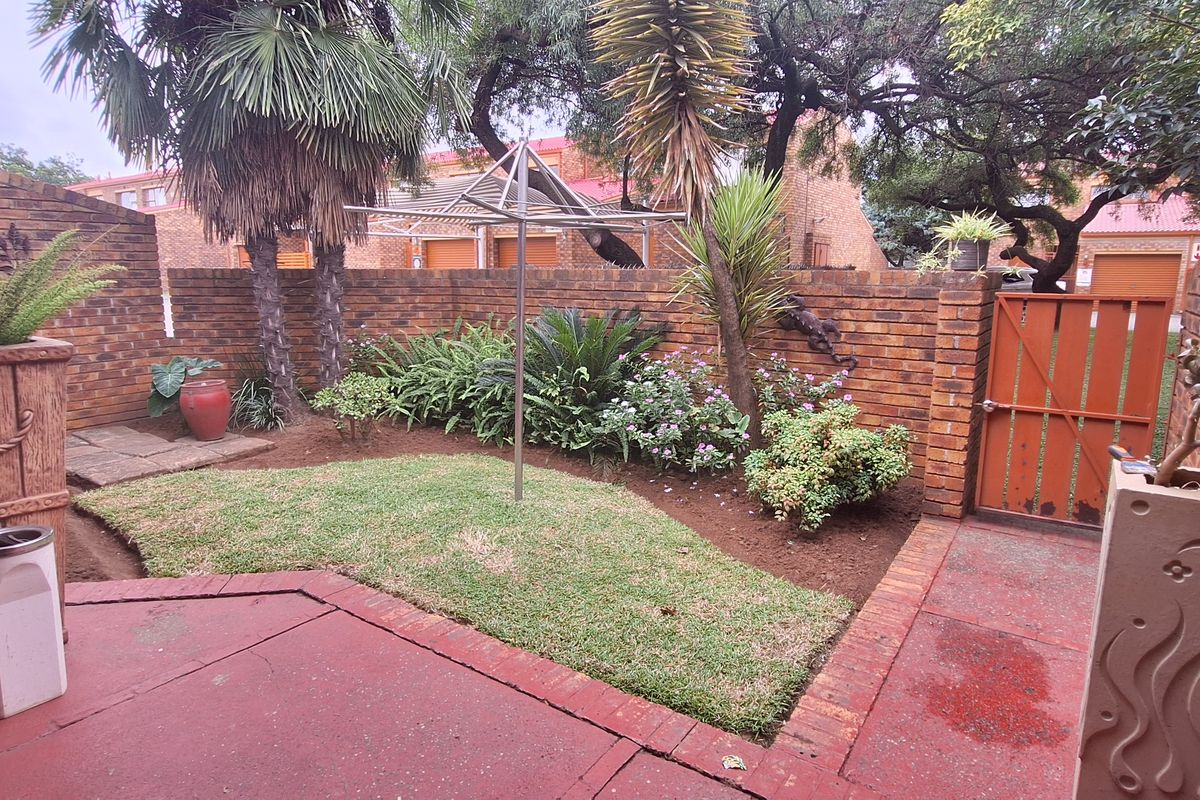 A private rear courtyard featuring a paved patio area, established garden beds, and a brick boundary wall with a secure gate.