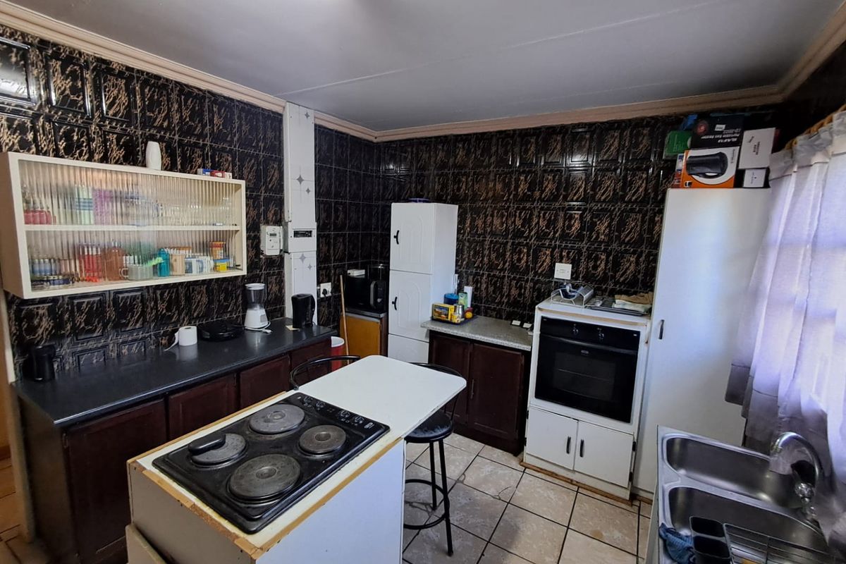 A dated kitchen featuring dark patterned wall tiles, built-in cabinetry, a standalone oven, and a central island with a built-in electric hob.