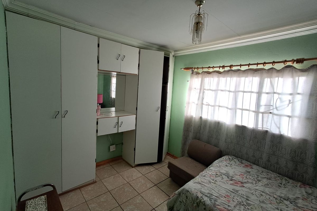 A bedroom featuring built-in wardrobes with an integrated vanity unit, tiled flooring, and a window with curtain rod.
