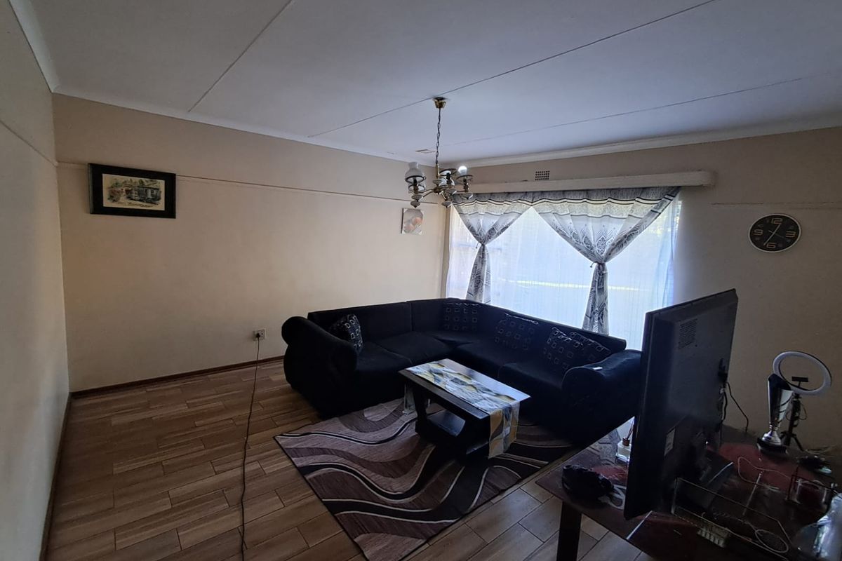 A living room featuring tiled flooring, a central light fixture, and a large window with curtain tracks.