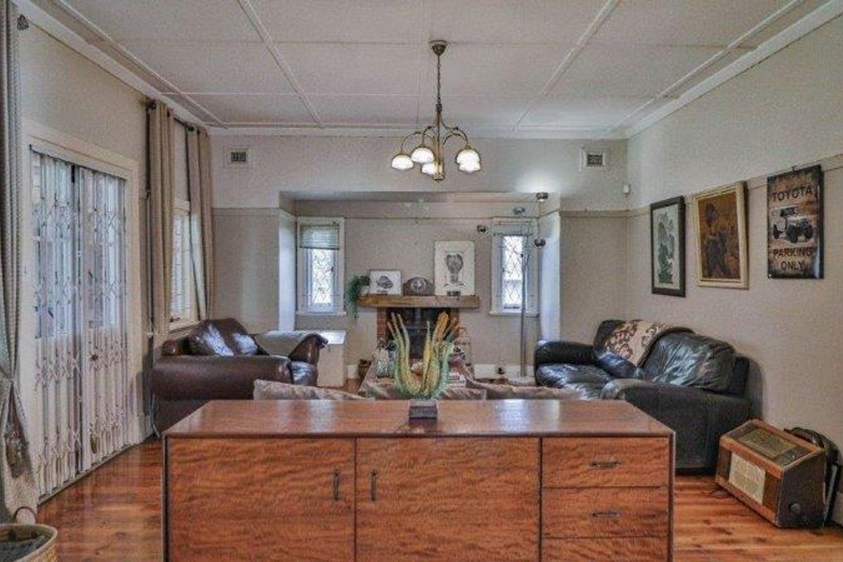 Spacious living room featuring original timber flooring, a central fireplace, and classic leaded glass windows, offering a traditional and character-filled atmosphere.