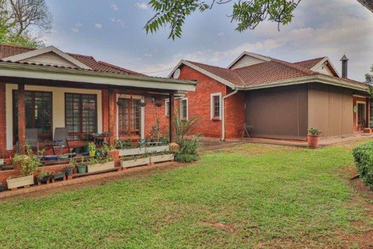 Rear view of a brick house featuring a covered patio area and a well-maintained lawn.