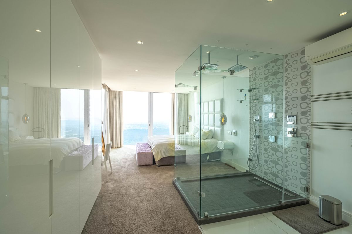 Modern open-plan bedroom suite featuring a glass-enclosed walk-in shower, built-in high-gloss wardrobes, and floor-to-ceiling windows with expansive views.