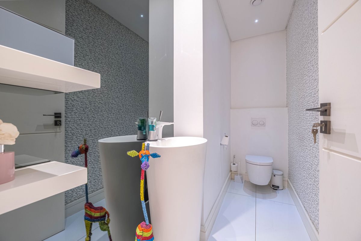 Modern guest bathroom featuring a sleek pedestal sink, wall-mounted toilet with concealed cistern, and textured wallpaper.