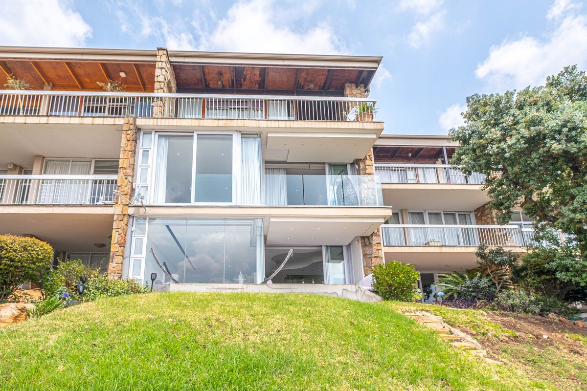 Rear elevation of a multi-story apartment building featuring tiered balconies, glass sliding doors, and stone-clad structural pillars overlooking a landscaped garden area.