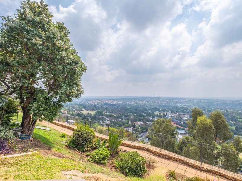 Elevated outdoor area featuring a stone-paved pathway, perimeter fencing, and expansive panoramic views over the surrounding landscape and city skyline.