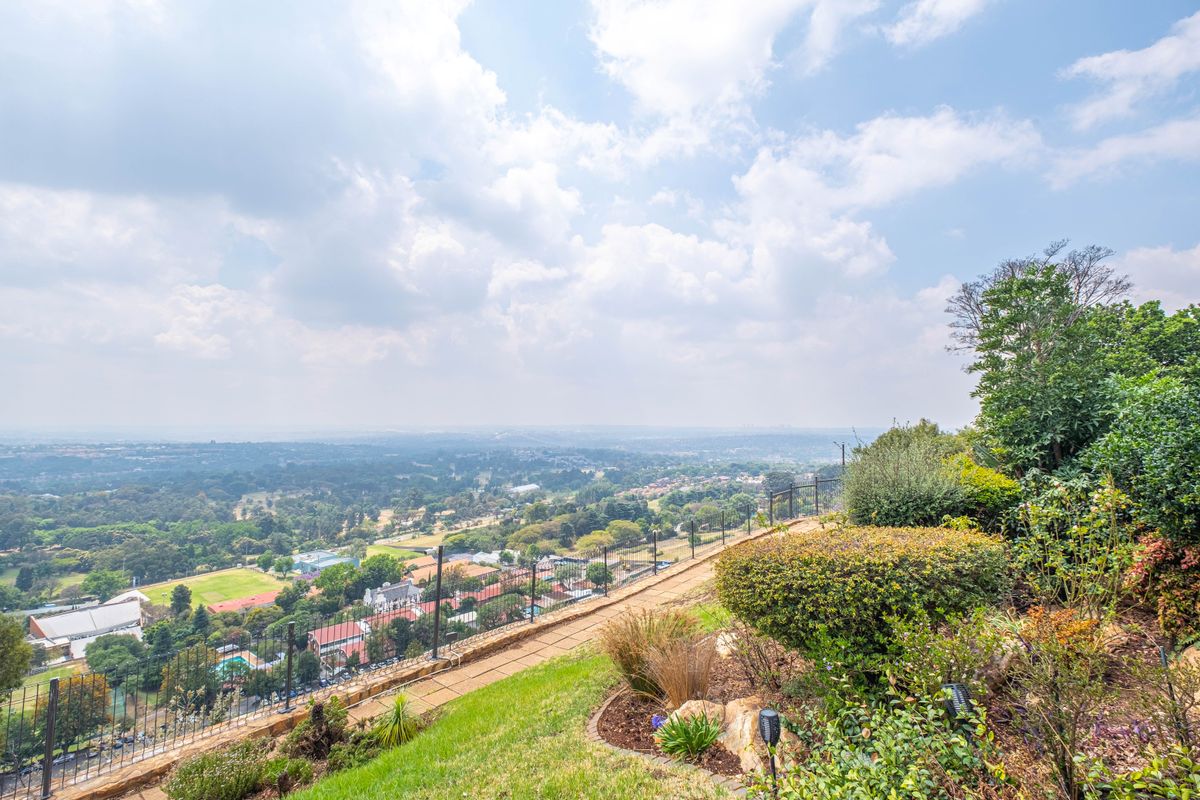 Elevated outdoor area featuring a landscaped garden, stone retaining wall, and metal perimeter fencing, offering expansive panoramic views of the surrounding landscape.