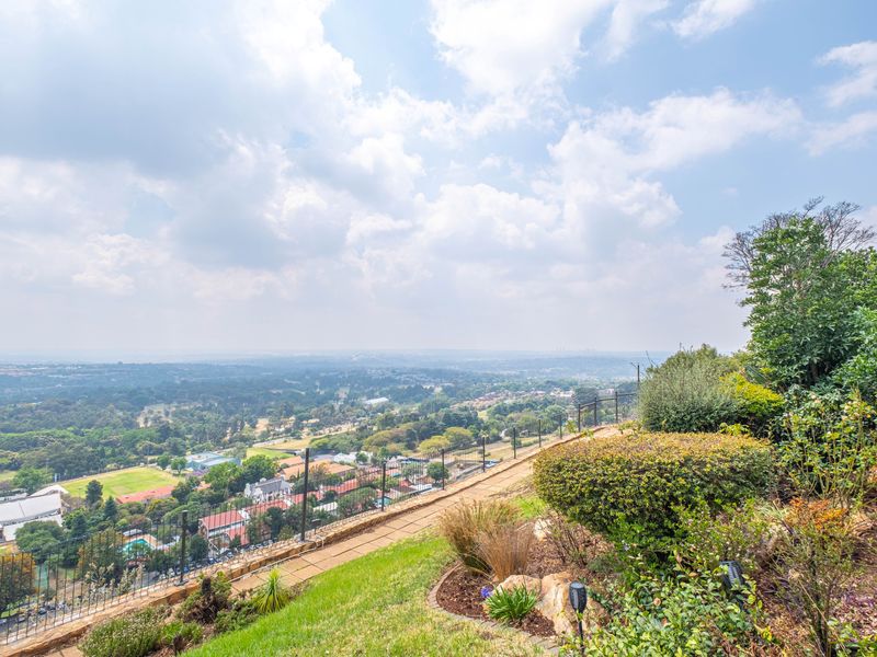 Elevated outdoor area featuring a landscaped garden, stone retaining wall, and metal perimeter fencing, offering expansive panoramic views of the surrounding landscape.