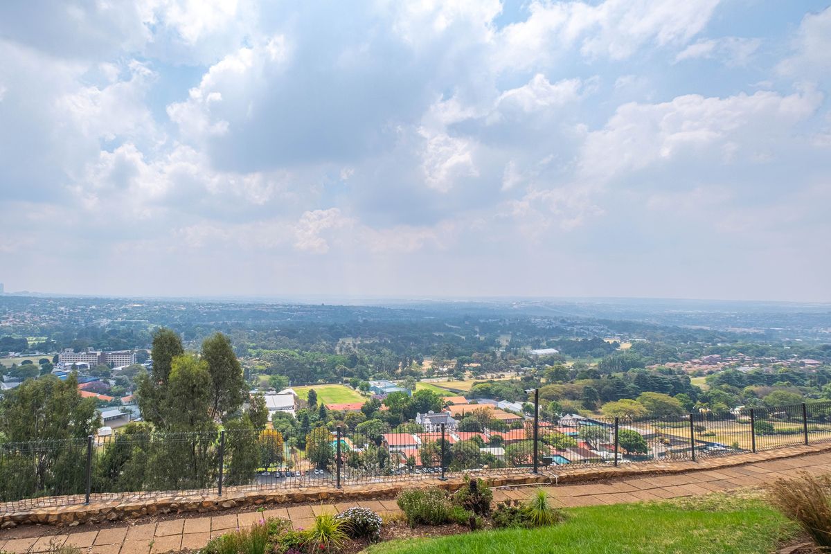 Elevated panoramic view overlooking the surrounding suburban landscape and greenery from a paved terrace with metal perimeter fencing.