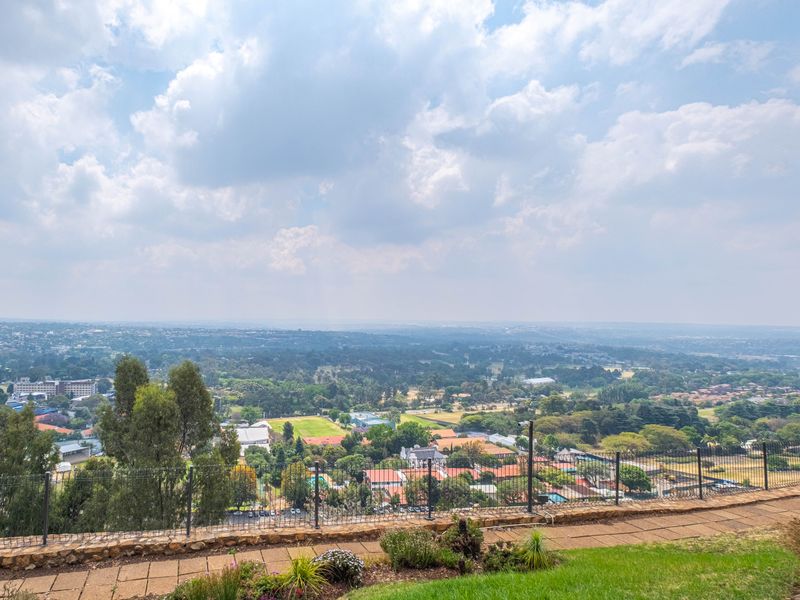 Elevated panoramic view overlooking the surrounding suburban landscape and greenery from a paved terrace with metal perimeter fencing.