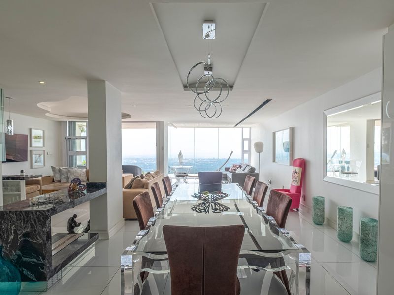Spacious open-plan dining and living area featuring polished tile flooring, recessed ceiling details, modern lighting, and expansive floor-to-ceiling windows with panoramic views.