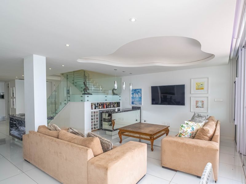Modern open-plan living area featuring a unique recessed ceiling design, glass-railed staircase, and a built-in bar area with integrated wine storage.