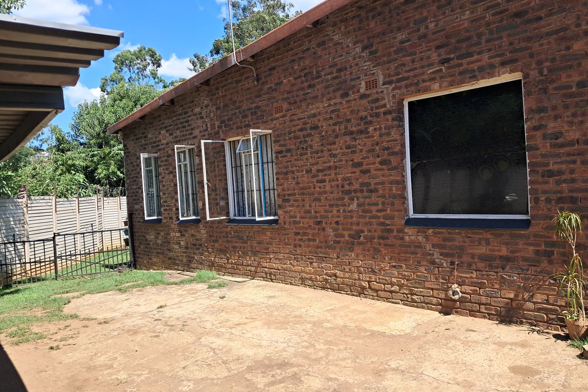 A view of the rear exterior of the house featuring exposed brick walls, security bars on windows, and a concrete patio area.