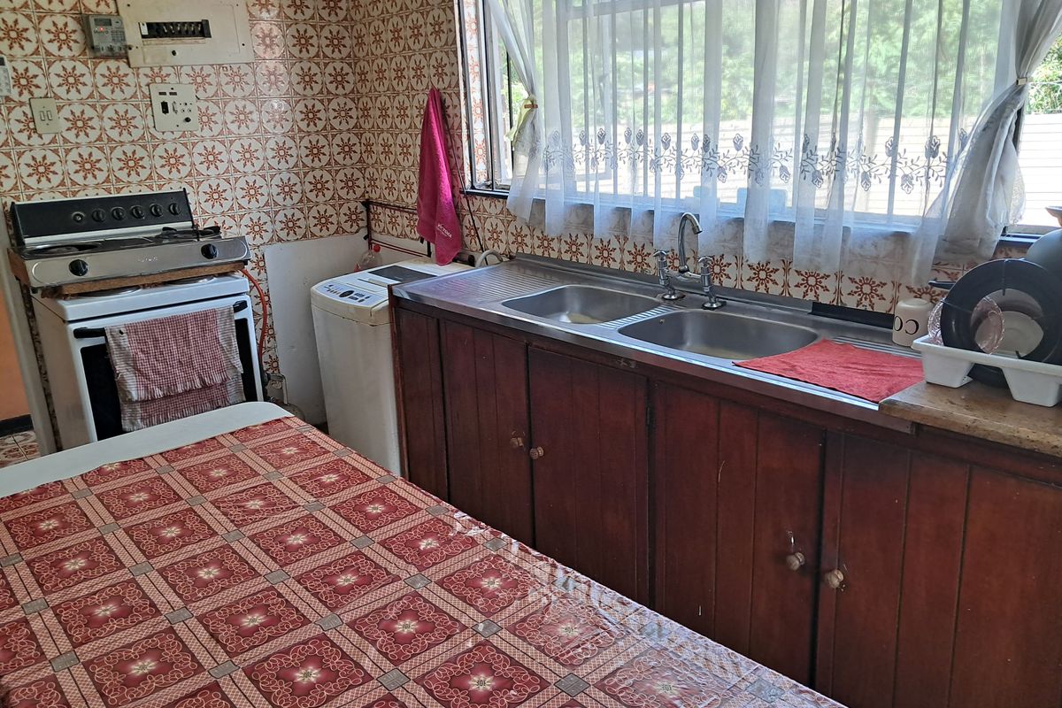 A dated kitchen featuring wooden cabinetry, a double stainless steel sink, and patterned wall tiles, offering a functional space with potential for modernization.