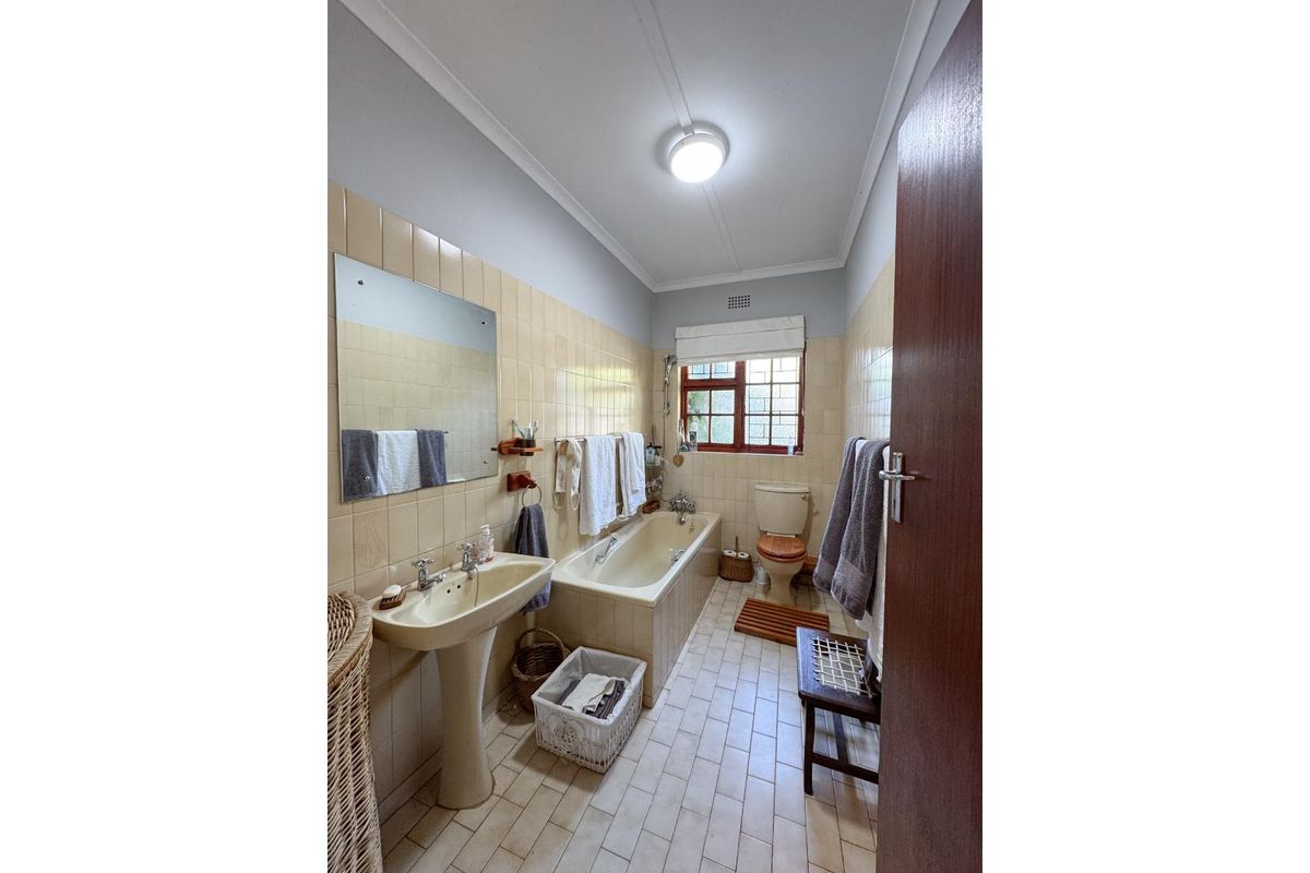 A dated bathroom featuring a pedestal basin, built-in bathtub, and toilet with original wall and floor tiling.
