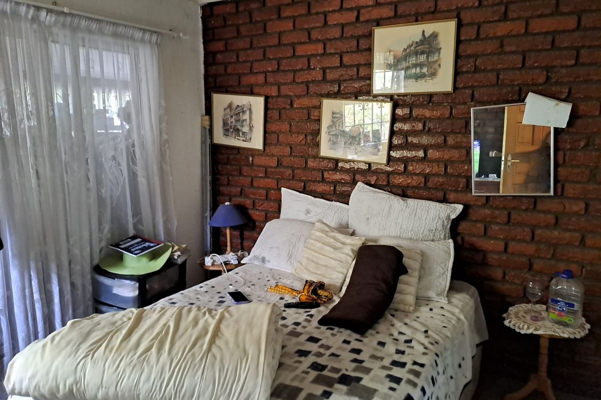 A bedroom featuring a prominent exposed brick feature wall and natural light from a window with sheer curtains.
