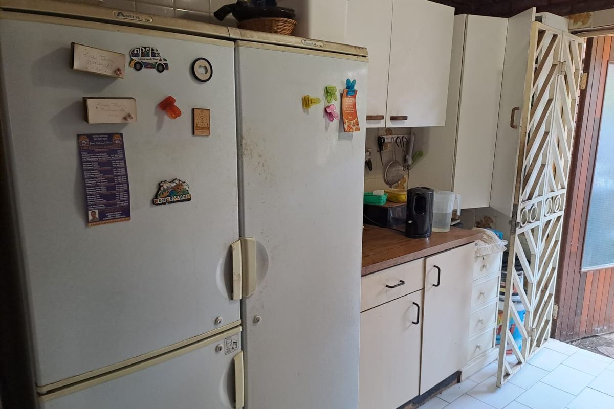 A dated kitchen area featuring built-in cabinetry, laminate countertops, and tiled flooring, requiring cosmetic updates to modernize the space.