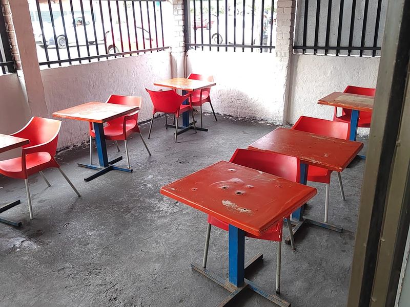 A covered outdoor patio area featuring concrete flooring, brick pillars, and metal security bars, suitable for an informal seating or entertainment space.