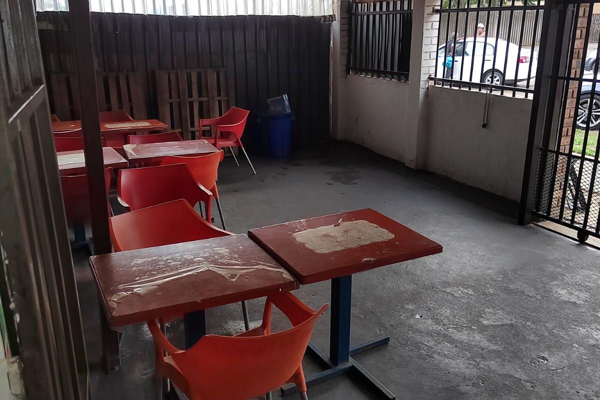 A covered outdoor patio area featuring concrete flooring, metal roofing, and security gate access, suitable for renovation or outdoor seating area improvements.