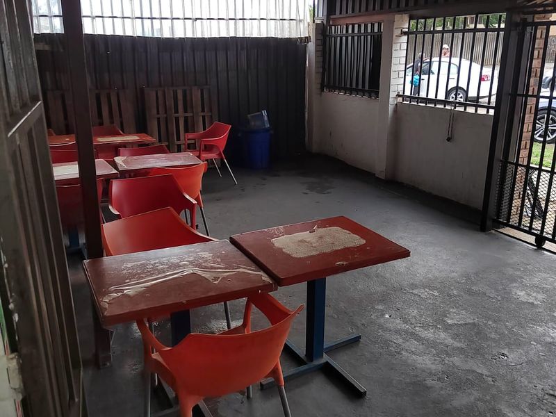 A covered outdoor patio area featuring concrete flooring, metal roofing, and security gate access, suitable for renovation or outdoor seating area improvements.