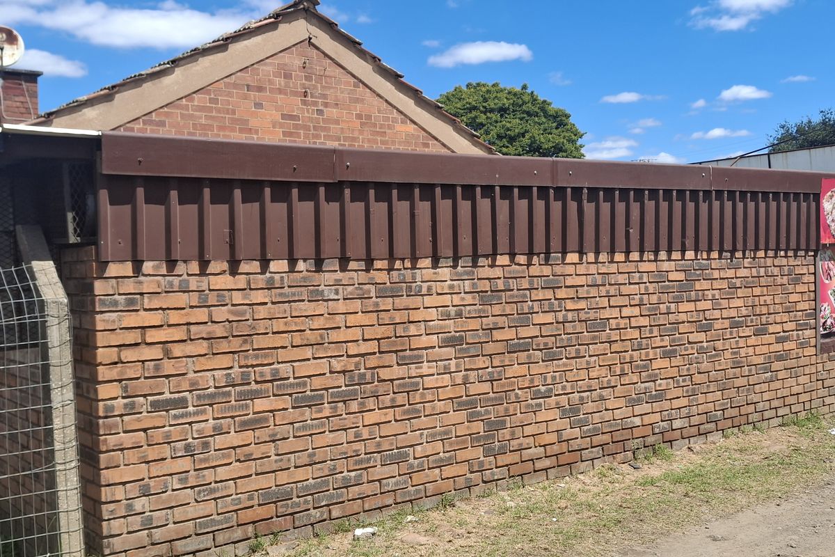 Exterior view of a brick building featuring a metal roof trim, chimney, and attached signage, showing signs of age and general wear.