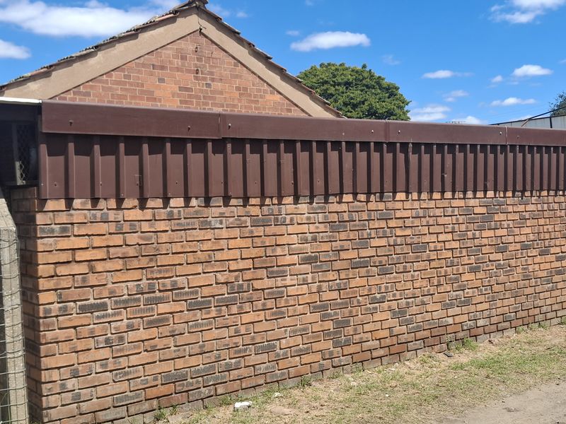Exterior view of a brick building featuring a metal roof trim, chimney, and attached signage, showing signs of age and general wear.