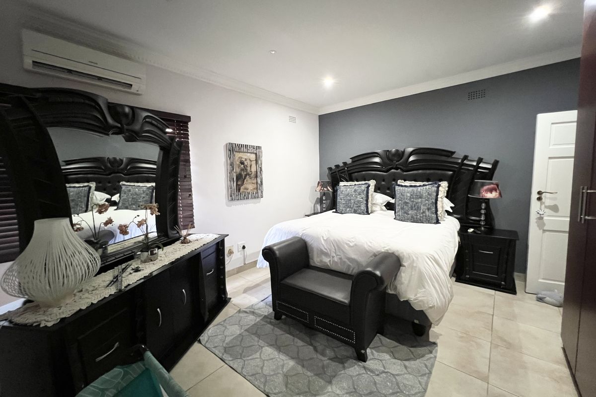 A well-maintained bedroom featuring tiled flooring, recessed downlighting, and a wall-mounted split-system air conditioning unit.