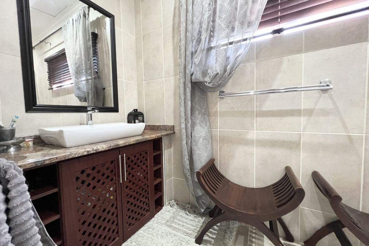 A well-maintained bathroom featuring a dark wood vanity cabinet, vessel sink, wall-mounted mirror, and neutral wall tiling.