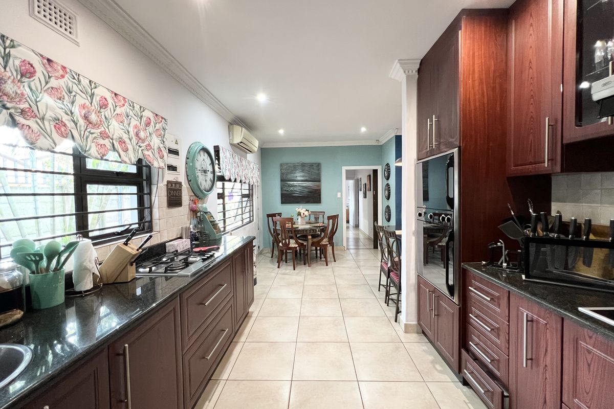 Spacious kitchen featuring dark wood cabinetry, granite countertops, gas hob, and built-in oven, flowing into an adjacent dining area with tiled flooring throughout.