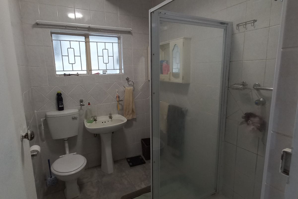 A functional bathroom featuring a pedestal basin, toilet, and a glass-enclosed shower with tiled walls and security bars on the window.