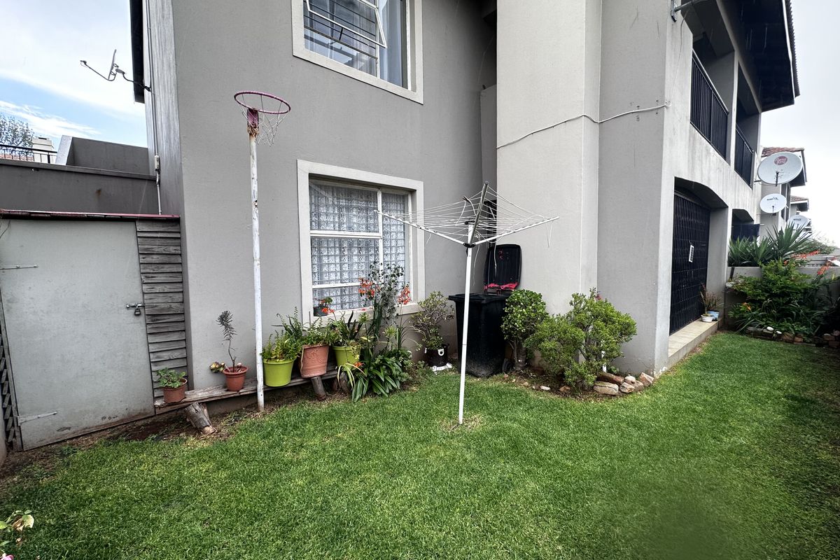 Rear exterior view of the apartment featuring a private lawn area, external storage shed, and established garden borders.