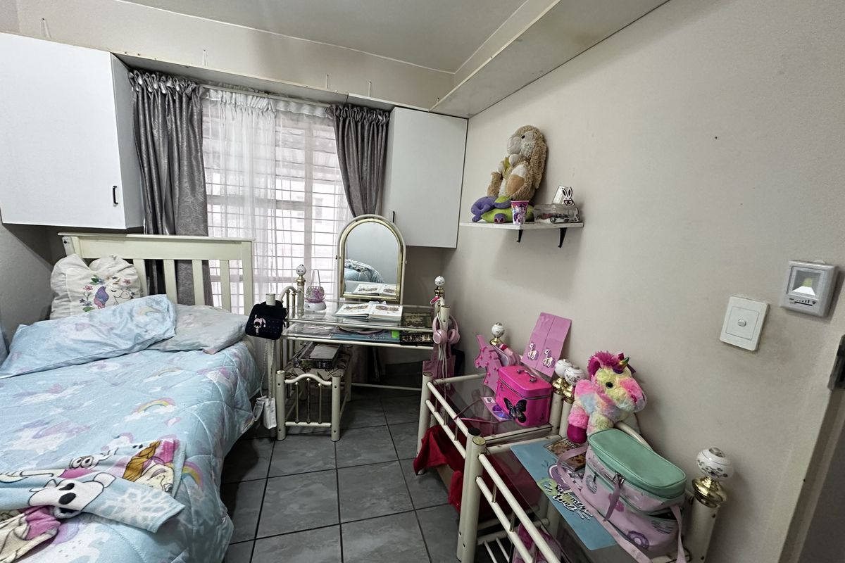 A compact bedroom featuring tiled flooring and built-in overhead storage cupboards, providing functional space for a single bed and vanity area.