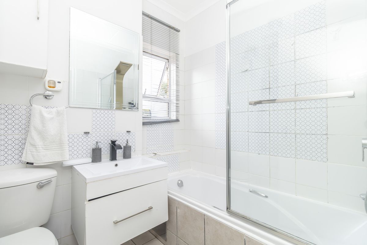 A functional bathroom featuring a vanity unit, a combined bathtub and shower with a glass screen, and tiled finishes.