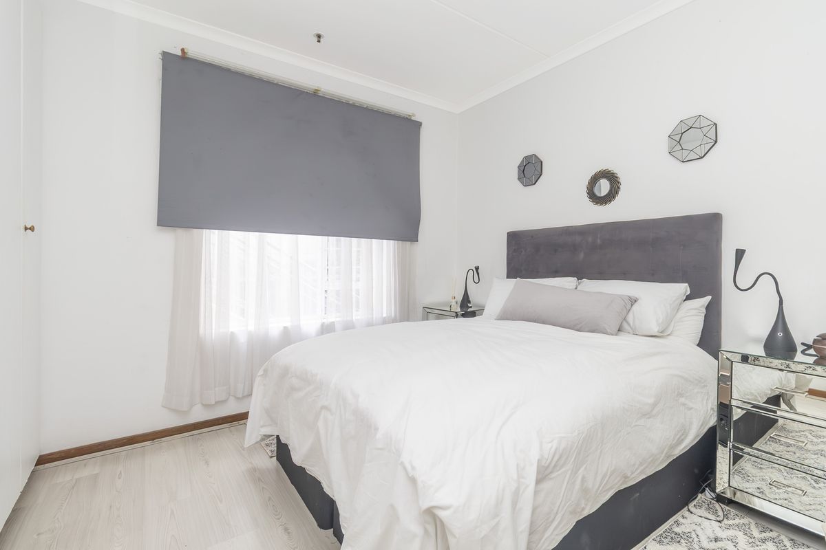 A well-lit bedroom featuring light-toned laminate flooring, neutral walls, and a built-in cupboard, offering a clean and comfortable living space.