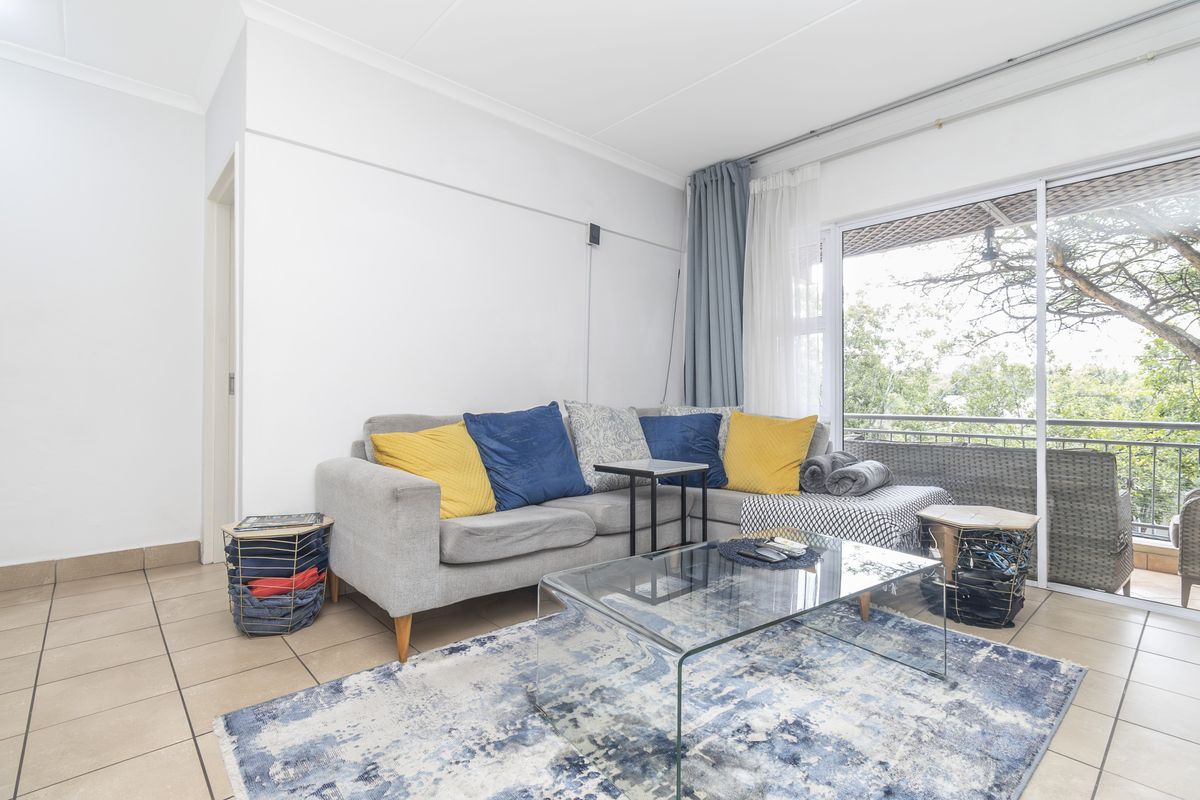 A bright living room featuring tiled flooring and a large sliding glass door providing access to an outdoor balcony area.