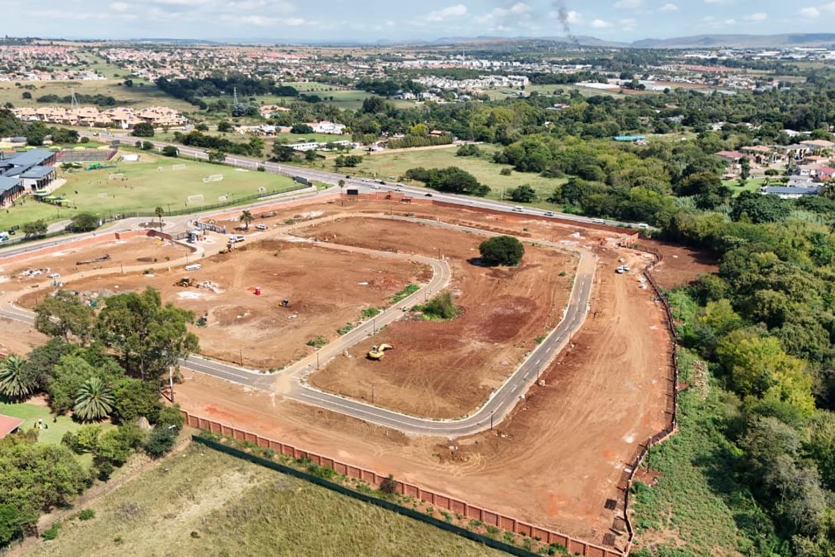 Aerial view of a residential development site featuring cleared land, internal paved roads, and perimeter fencing in a suburban setting.