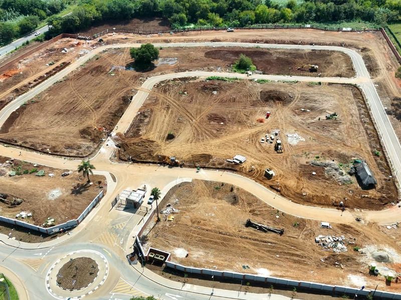 Aerial view of a residential development site showing cleared land, internal road infrastructure, perimeter fencing, and a security entrance gatehouse.
