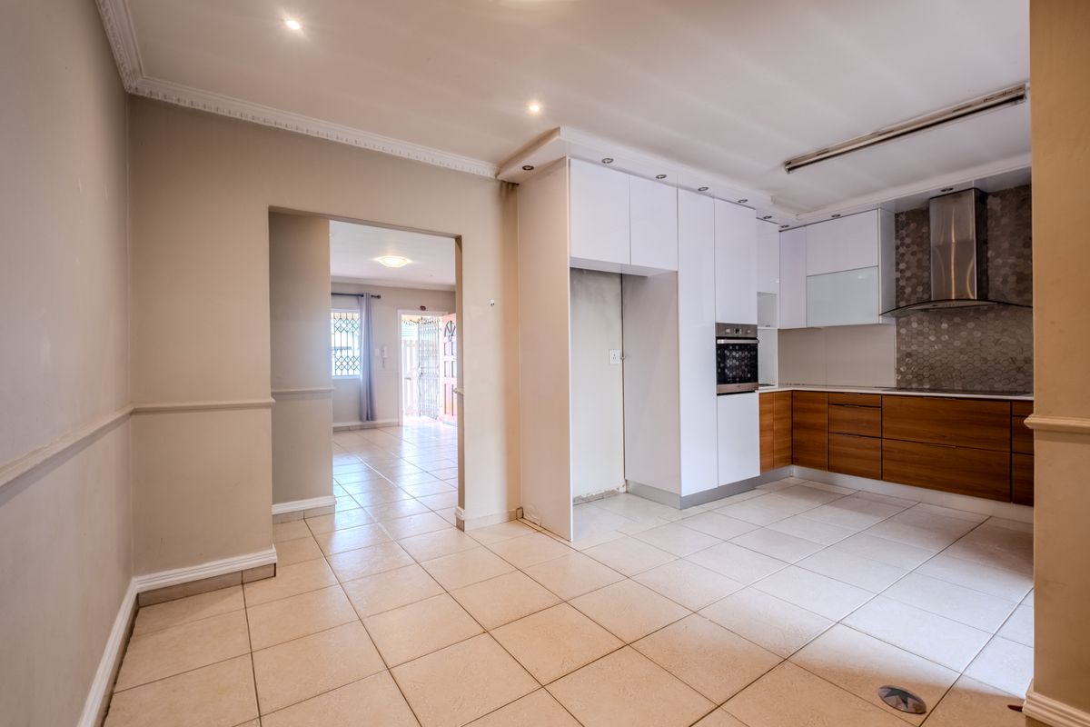 Modern kitchen featuring two-tone cabinetry, built-in oven, extractor fan, and mosaic backsplash, with tiled flooring and recessed lighting throughout the open space.