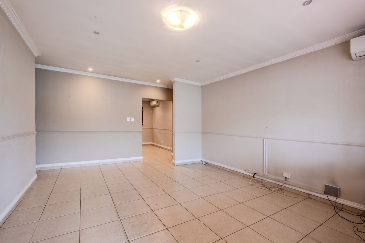 An empty, open-plan living area featuring neutral tiled flooring, crown molding, chair rail detailing, and a wall-mounted air conditioning unit.
