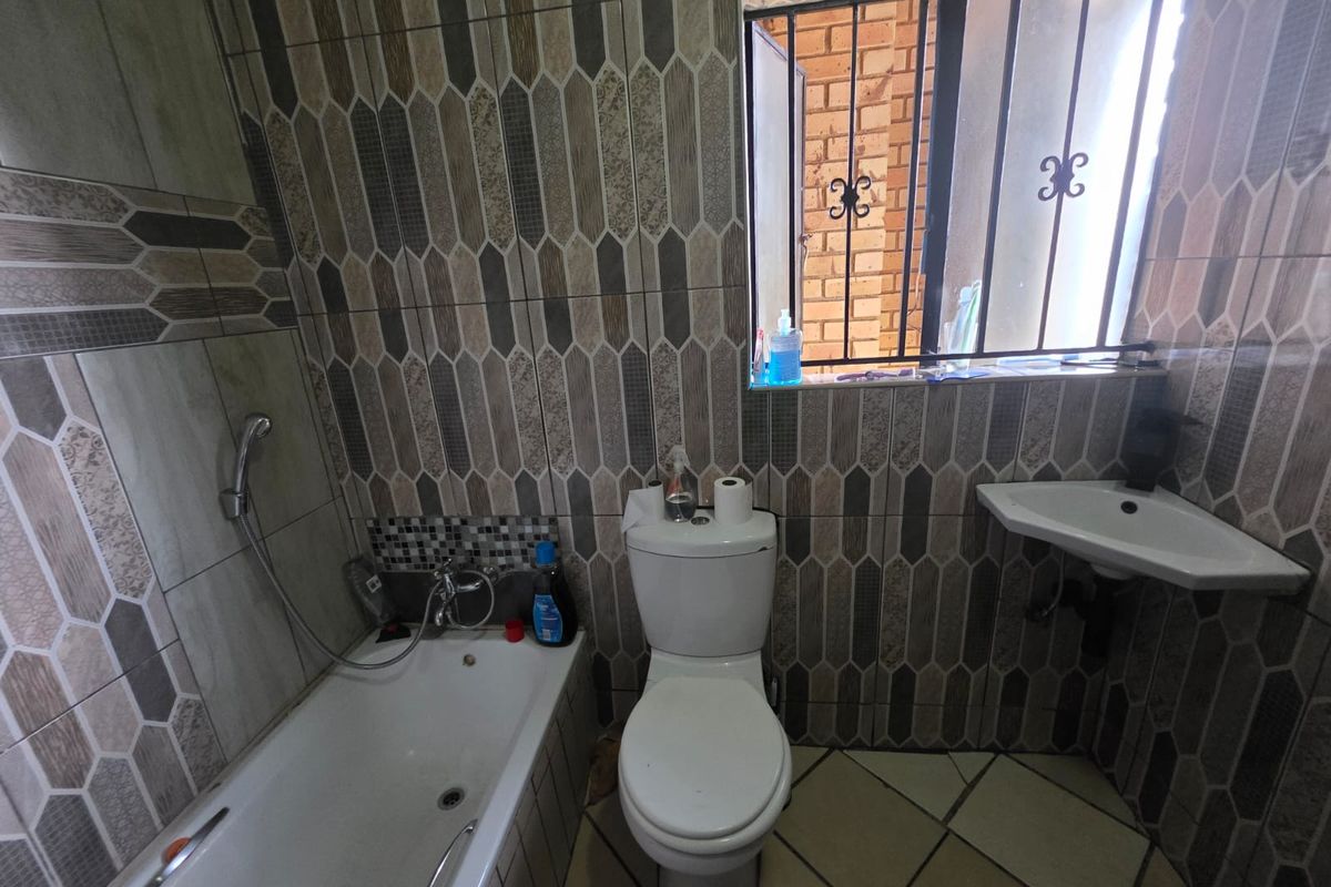 A compact bathroom featuring a bathtub with handheld shower attachment, a standard toilet, and a corner-mounted wall basin with decorative wall tiling.