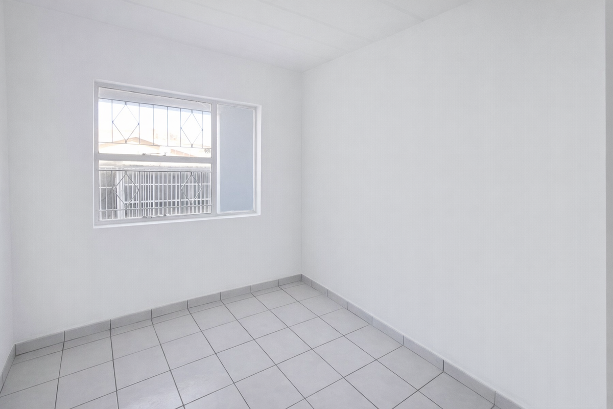 A clean, empty bedroom featuring neutral tiled flooring and a window fitted with security bars.