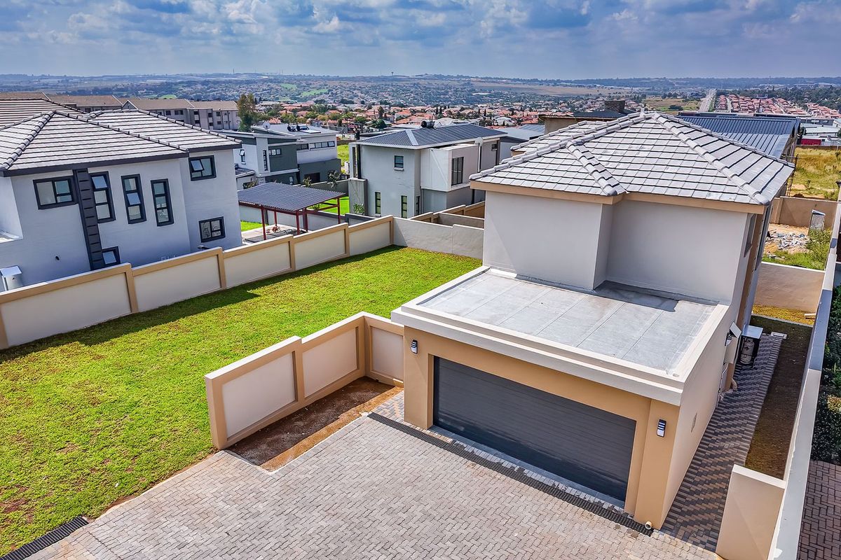 Aerial view of a residential property featuring a paved driveway, a single garage, and a private lawn area enclosed by boundary walls.