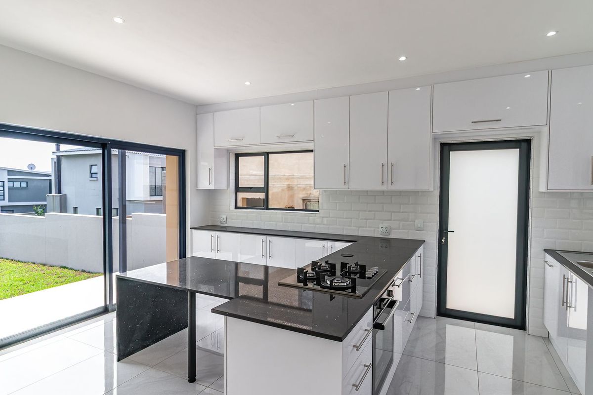 Modern kitchen featuring white cabinetry, black stone countertops, integrated gas hob, built-in oven, and large sliding glass doors leading to the garden.