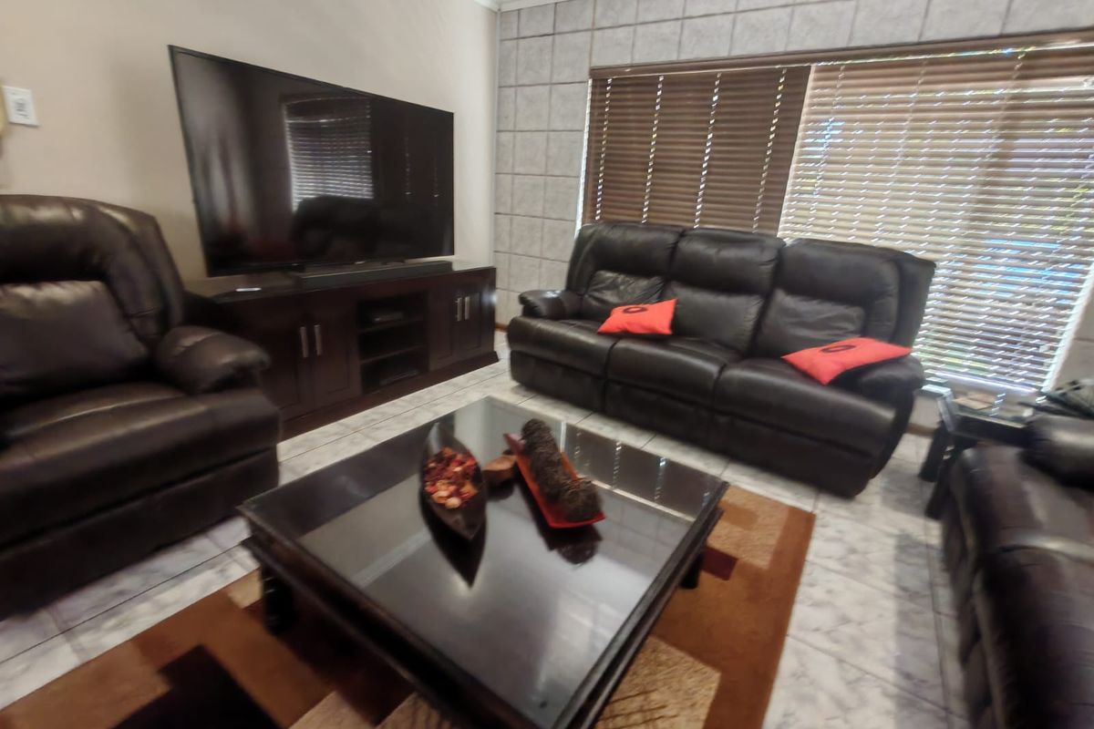 A comfortable living room featuring tiled flooring, decorative wall paneling, and venetian blinds, providing a functional space for relaxation.