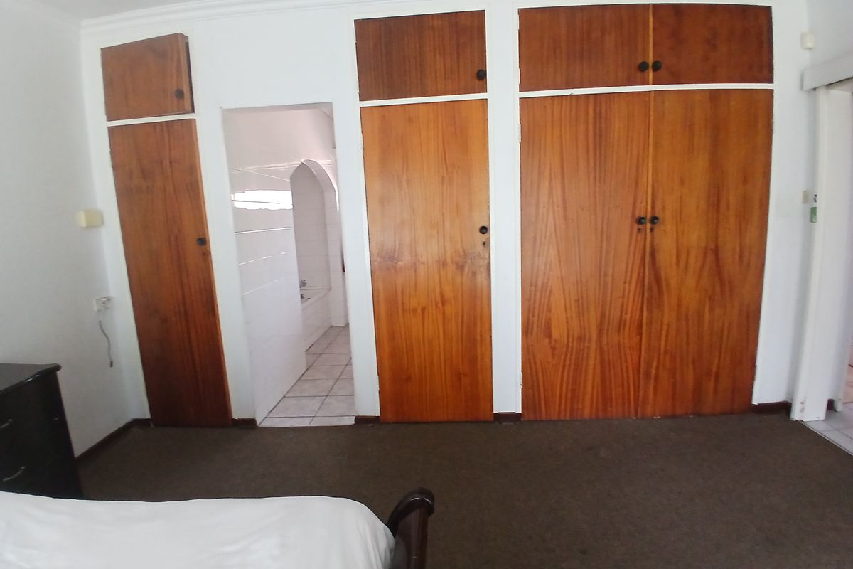 Bedroom featuring extensive built-in wooden cabinetry and direct access to an en-suite bathroom, offering a functional layout with potential for modern updates.