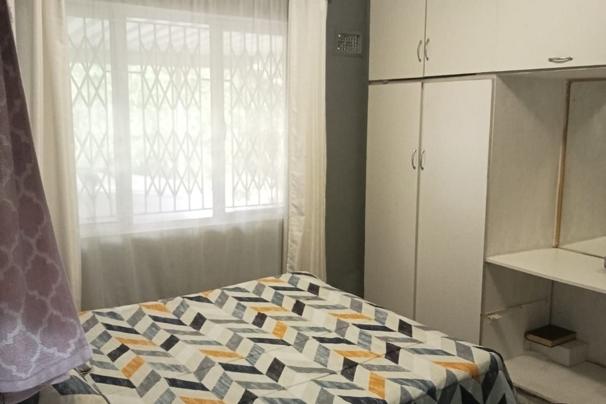 A functional bedroom featuring built-in cupboards, a vanity area, and a security gate on the window.