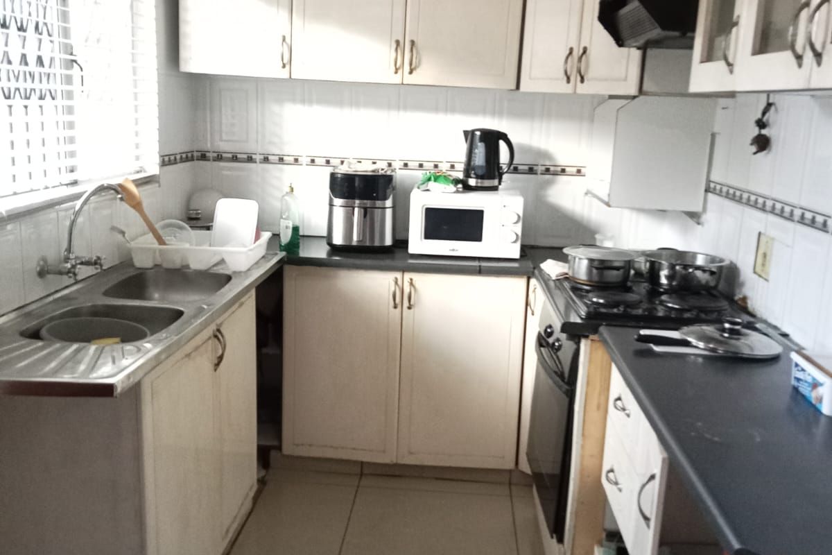A functional kitchen featuring built-in cabinetry, a double bowl sink, tiled splashbacks, and integrated cooking appliances, offering potential for cosmetic updates.