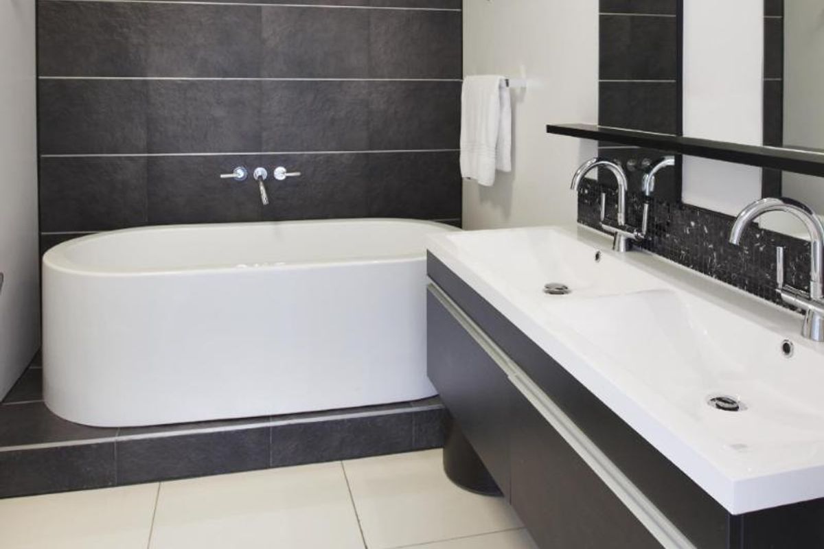 Modern bathroom featuring a sleek freestanding bathtub, a double vanity with integrated sinks, and contemporary dark tile finishes.